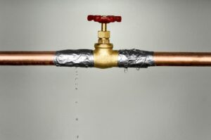 A makeshift repair on a leaking copper pipe with duct tape, failing to stop the drip completely under a closed faucet.