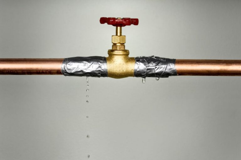 A makeshift repair on a leaking copper pipe with duct tape, failing to stop the drip completely under a closed faucet.