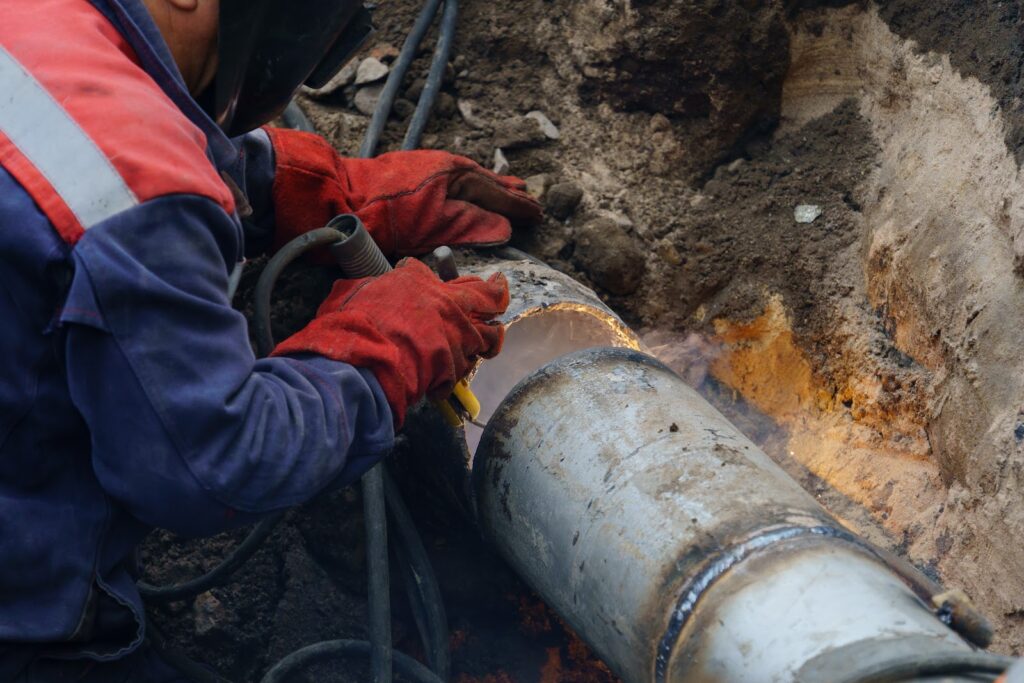 A worker is working on a pipe in the ground.