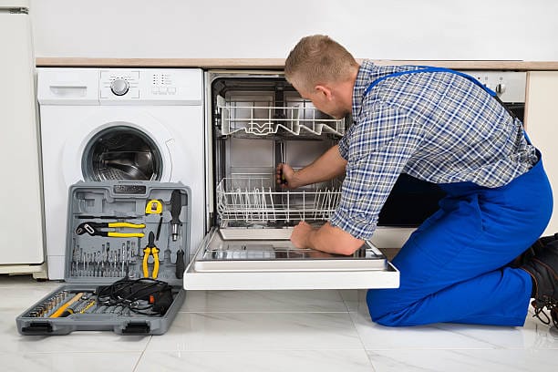 A man fixing a dishwasher in a kitchen.